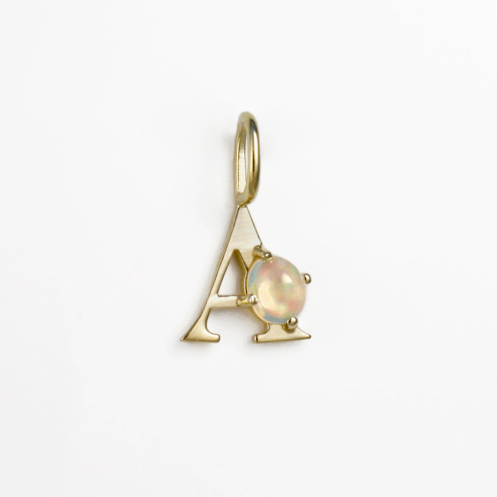 This A monogram 14k gold charm has a crystal opal incorporated into its structure.