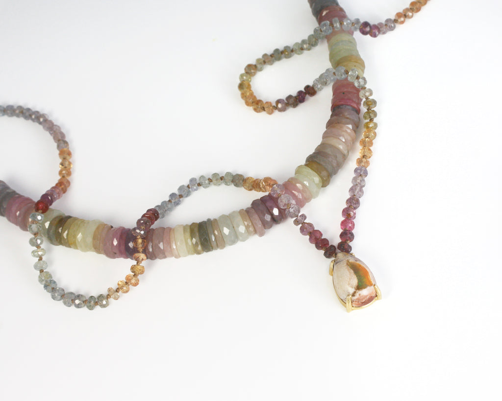 A magical treasure from nature, this necklace highlights a pear-shaped boulder Mexican opal, with a captivating display of green, yellow, and orange fire glowing at its center. Strung on silk thread, the opal is complemented by a vibrant array of multicolor Songea sapphires, adding warmth and vibrancy. A unique piece with an organic feel.&nbsp;