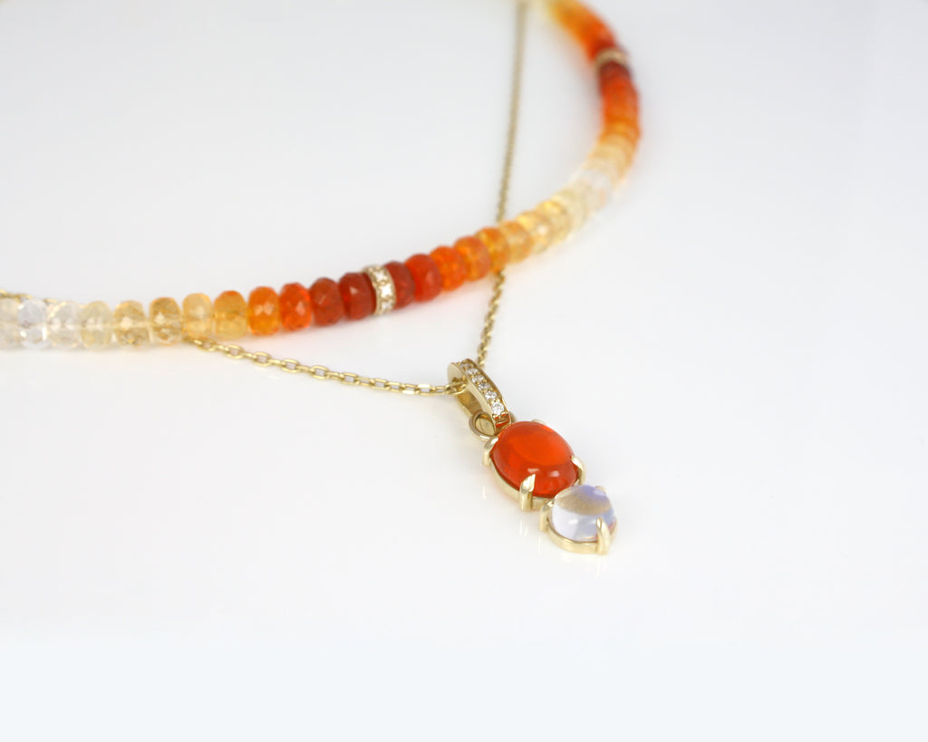A vivid fire opal paired with a mystic moonstone forms a luminous charm, suspended from a sparkly cable chain. The charm is connected by a hinged bail accented with diamonds, adding a touch of brilliance to this radiant, ethereal piece.