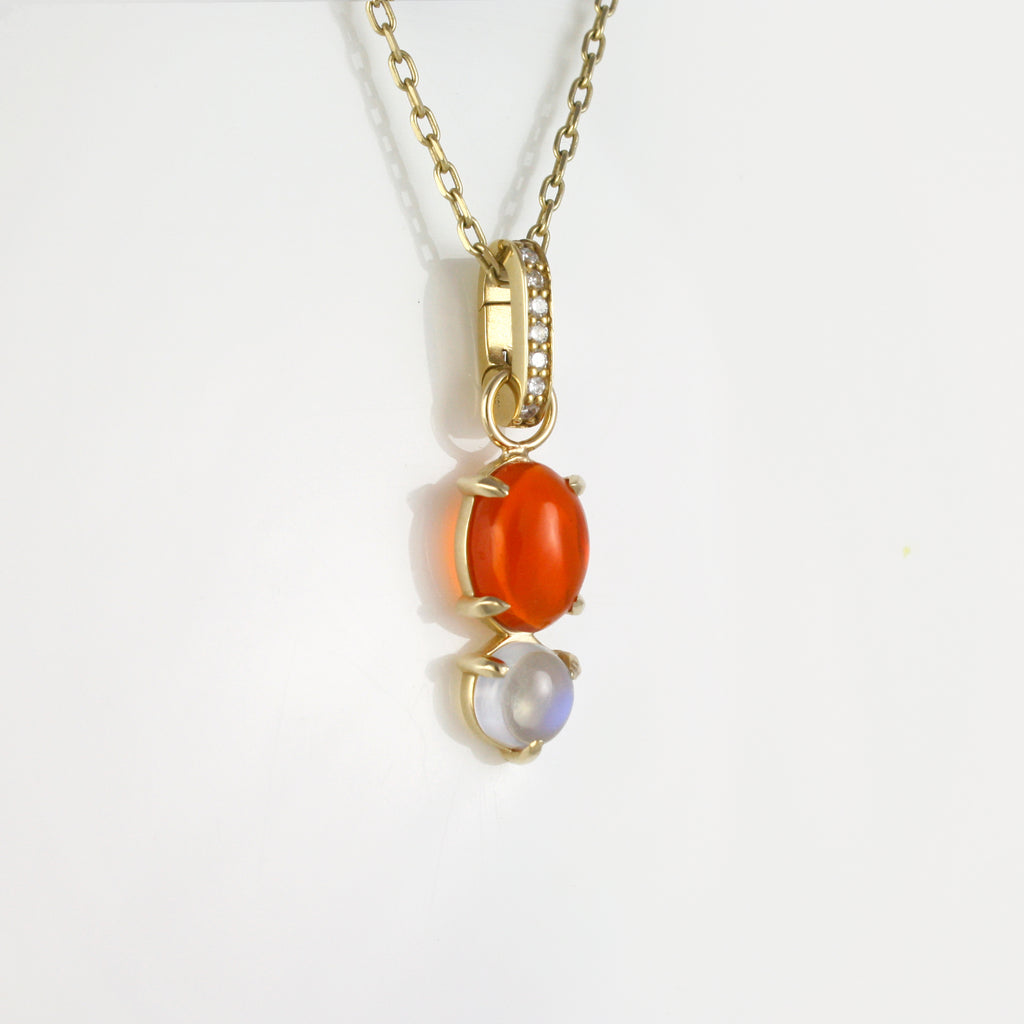 A vivid fire opal paired with a mystic moonstone forms a luminous charm, suspended from a sparkly cable chain. The charm is connected by a hinged bail accented with diamonds, adding a touch of brilliance to this radiant, ethereal piece.