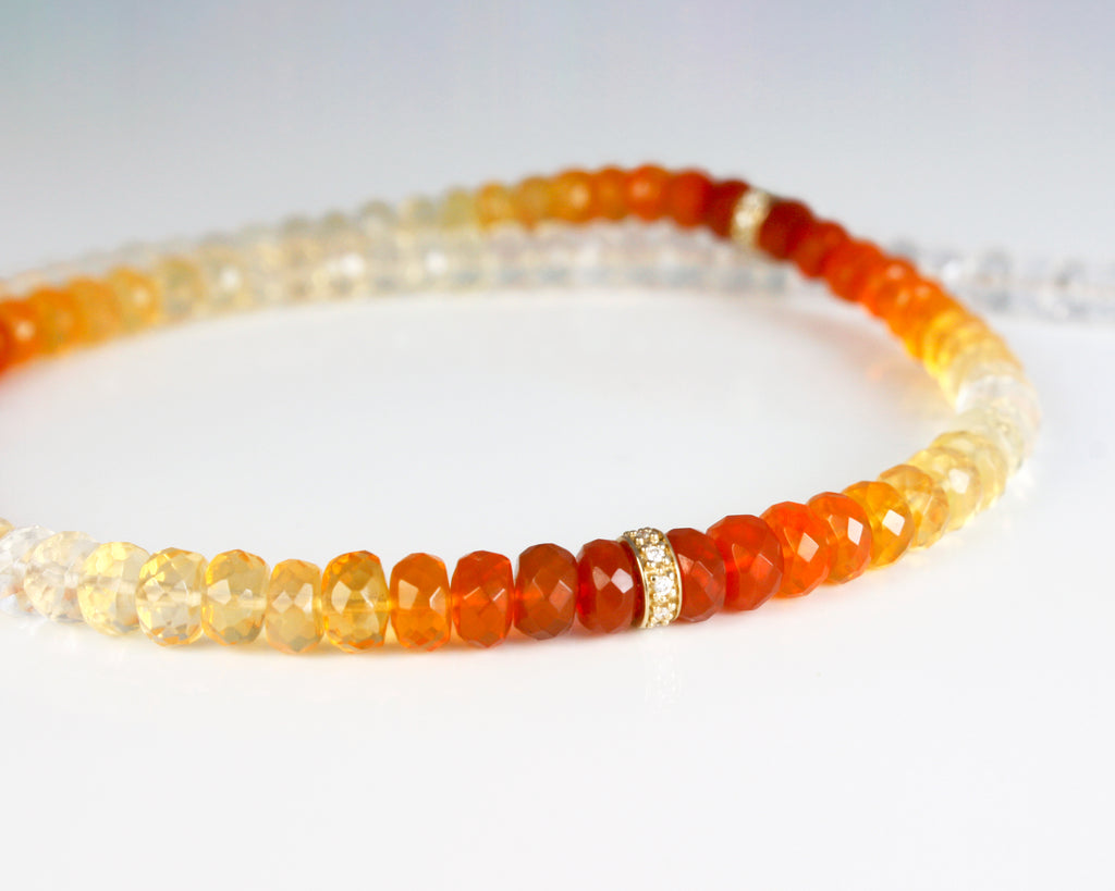 This exquisite necklace features a stunning arrangement of fire opals, gradually transitioning from a vivid fiery red to a delicate transparency, creating a captivating gradient effect. Interspersed between the opals are sparkling roundels of diamonds and gold, adding a brilliant contrast to the warm, glowing hues of the opals.