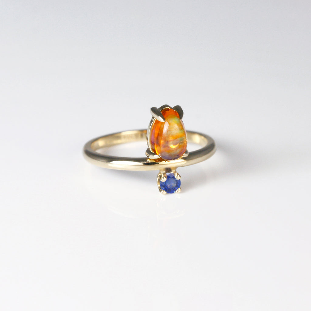This unique ring has an understated yet eye-catching vibe. It features a Mexican opal with blue and green fire that dances with light. On the other side, a vivid blue sapphire adds a beautiful contrast, making the opal's colors pop.