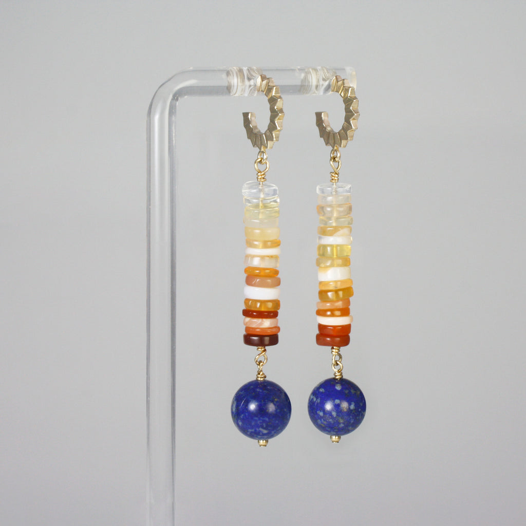 Inspired by the sun—the Aztec symbol of the god&nbsp;Tonatiuh—these bold dangle earrings feature heishi-cut ombré opals that flow in a radiant gradient from clear to fiery orange-red. Anchoring the piece is a round-cut, vibrant lapis lazuli stone. Daring, unique, and full of light.