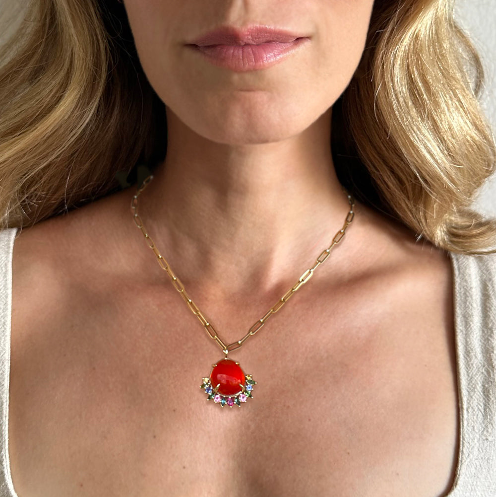 A large and vibrant Mexican fire opal with an intense orange-red hue is paired with tourmalines, iolites, and citrines, all set in 14k gold. This unique charm, hanging from a bold paperclip chain, makes for an eye-catching piece and a true conversation starter.