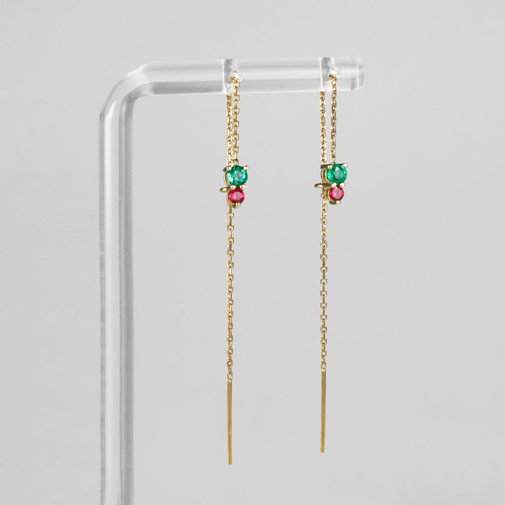 A lively emerald and ruby, beautifully contrasted, dangle at the end of a sparkling gold chain