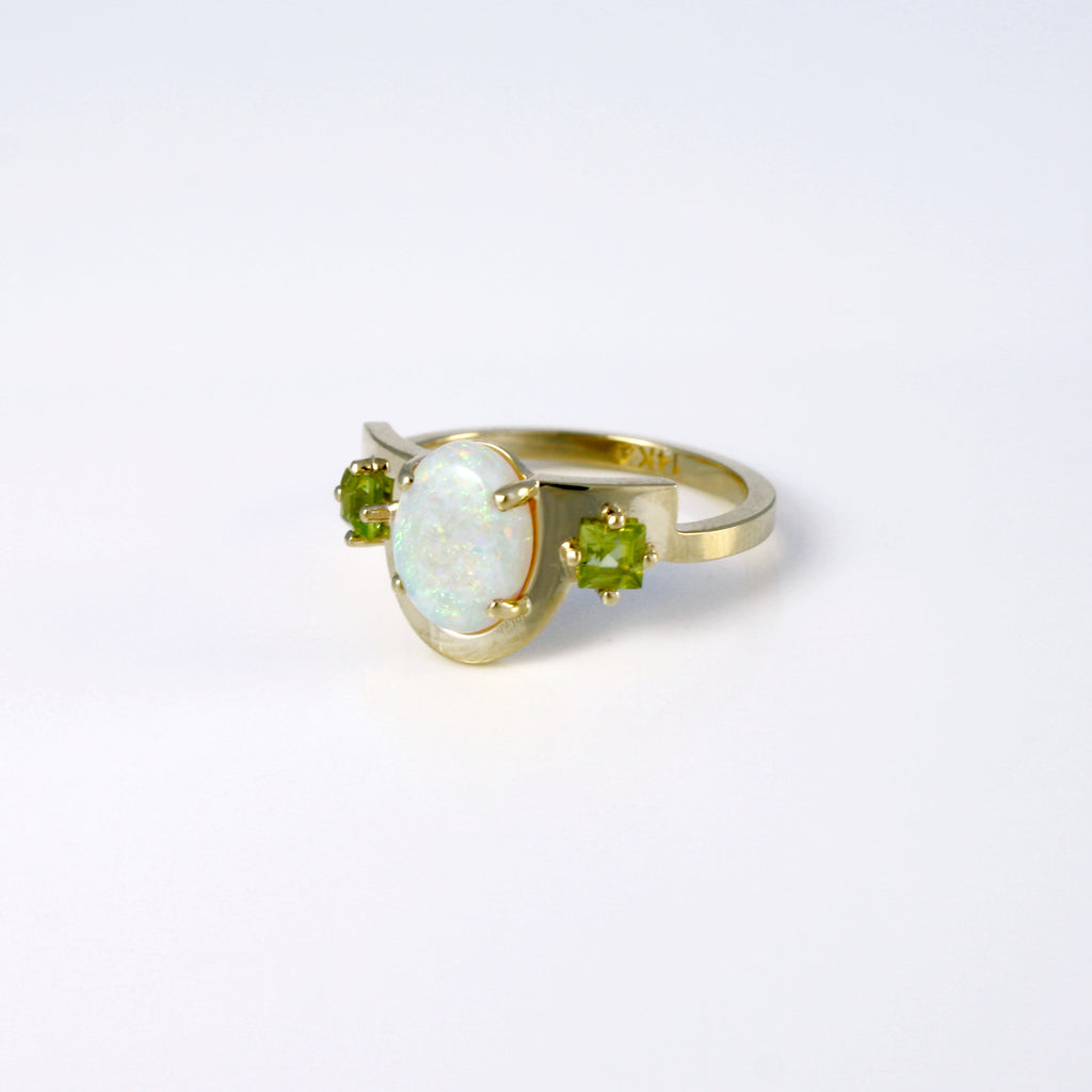 A soft geometric line that elegantly borders a stunning Mexican white opal with a vibrant peridot on each side. 